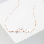 The Heartbeat Necklace in rose gold features a heartbeat and heart-shaped pendant on a white background—perfect as a unique, personalized gift.
