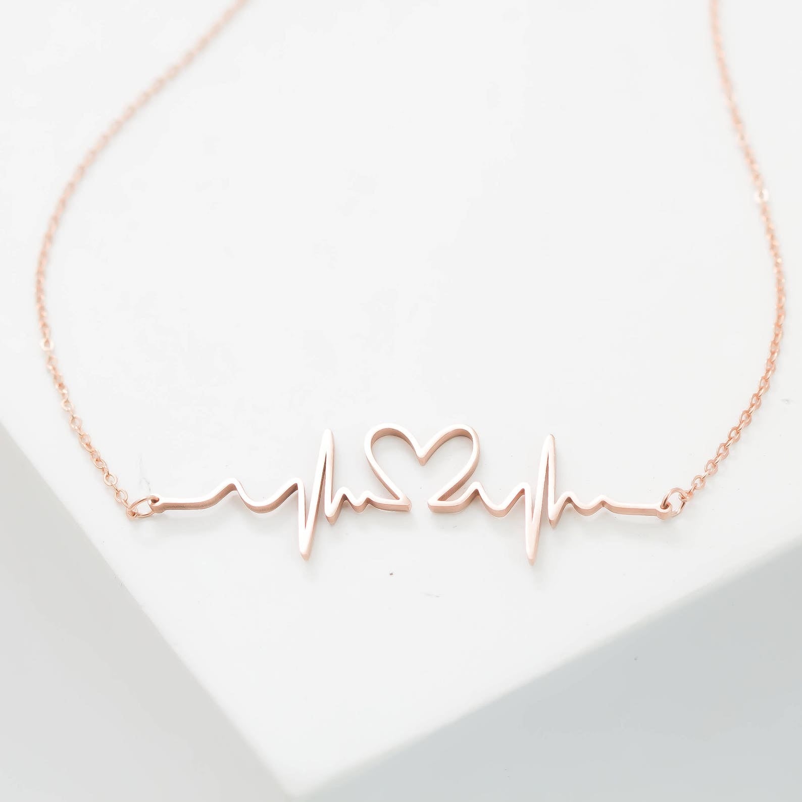 The Heartbeat Necklace in rose gold features a heartbeat line with a central heart, shown on a white background—a unique, personalized gift for someone special.
