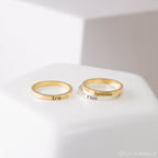 Three Stacking Name Bands—two gold and one silver—engraved with Tris, Jasmine, and Finn rest on a white surface, perfect for creating a personalized stackable ring set.