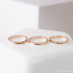 The Stacking Name Band features three gold stackable rings engraved with Charlotte, Jasper, and Best Nana—each personalized for a thoughtful keepsake, elegantly displayed on a white surface.