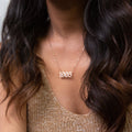 A woman wearing the Year Necklace featuring "1995" in gold, paired with a textured beige top.