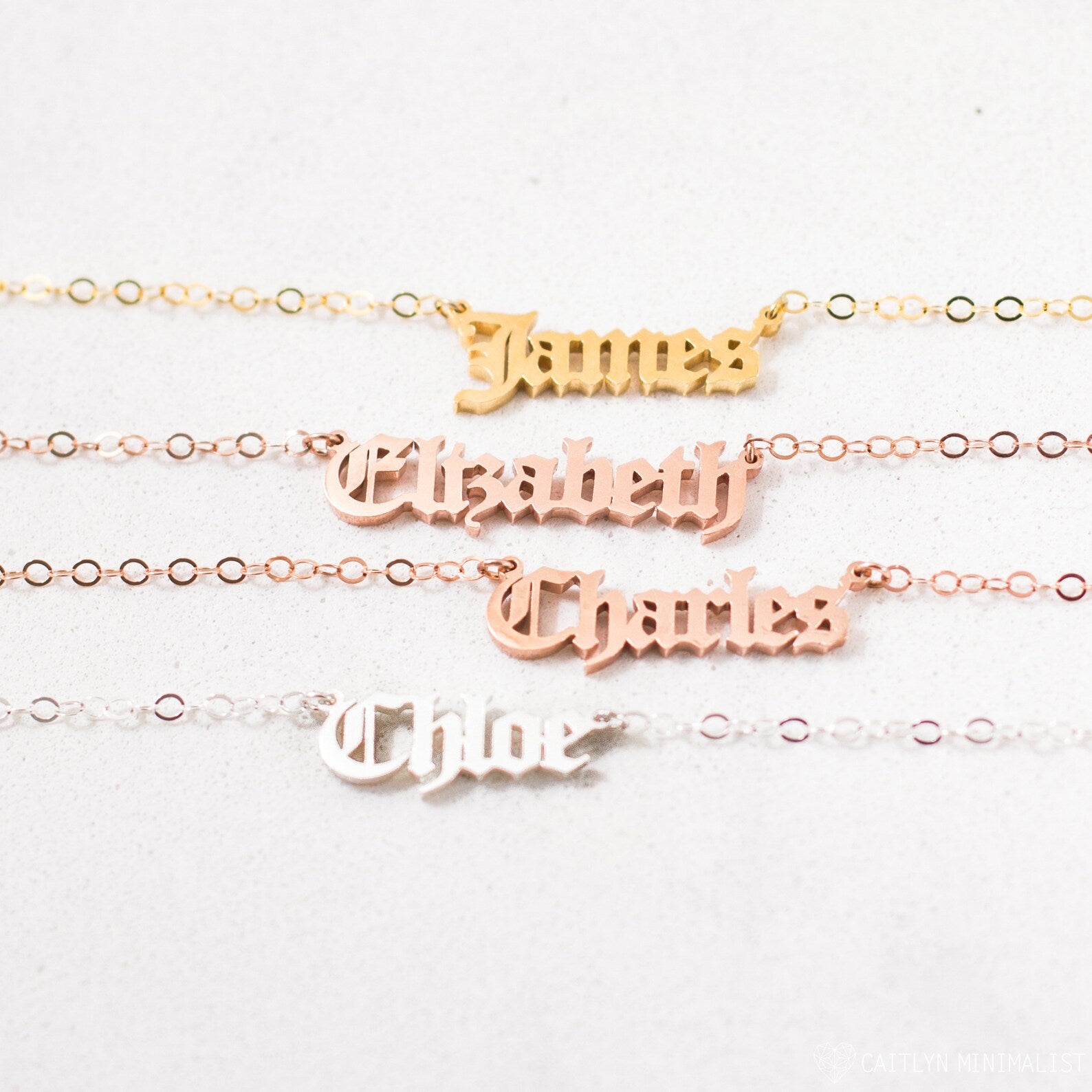 Four Old English Name Necklaces in gold, rose gold, and silver display the names James, Elizabeth, Charles, and Chloe—each a personalized charm.