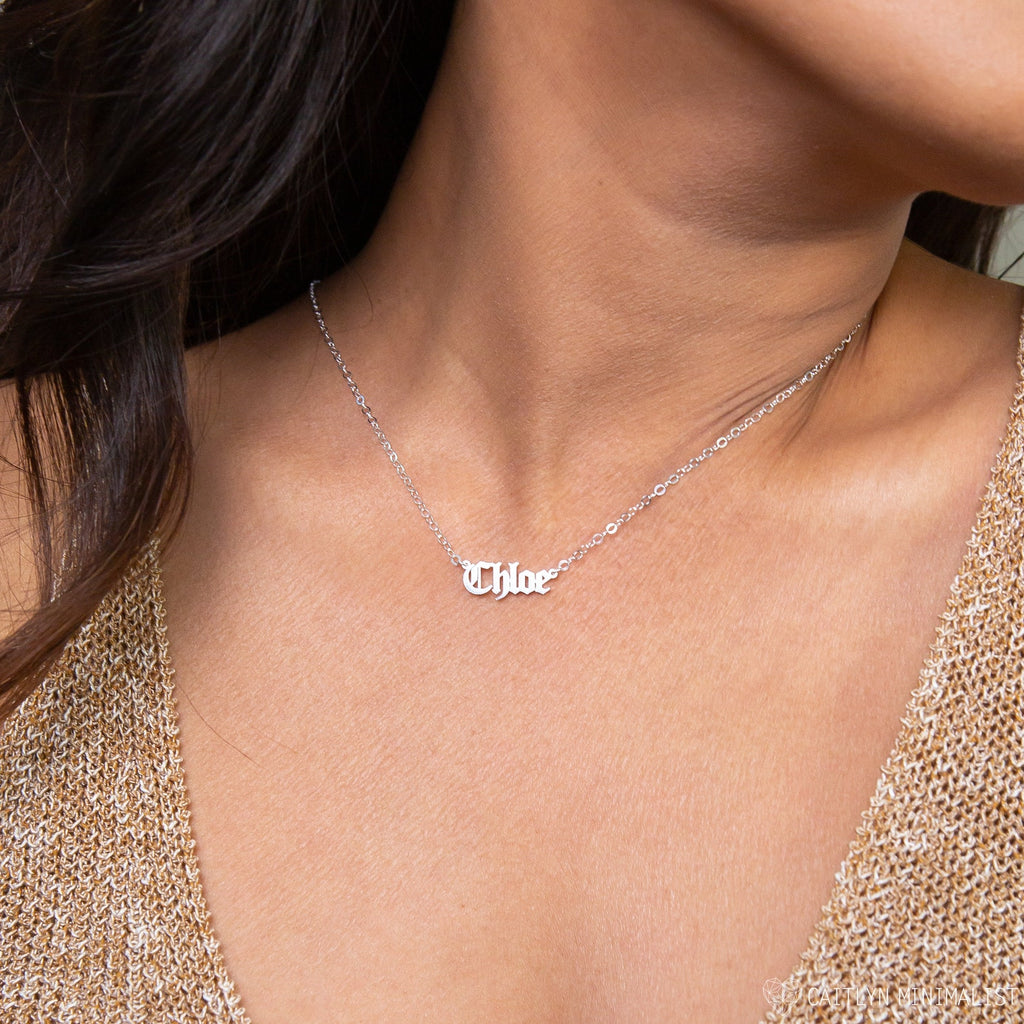 A woman wearing an Old English Name Necklace in silver, personalized with the name Chloe in elegant script.