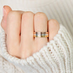 A hand wearing a white knitted sweater displays three stacked Stacking Name Band rings, each engraved with names.