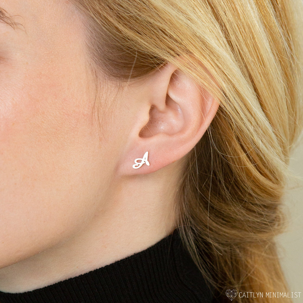 Close-up of a woman's ear adorned with the Alex Initial Studs, delicate earrings shaped like the letter A—ideal for lovers of personalized initial jewelry.
