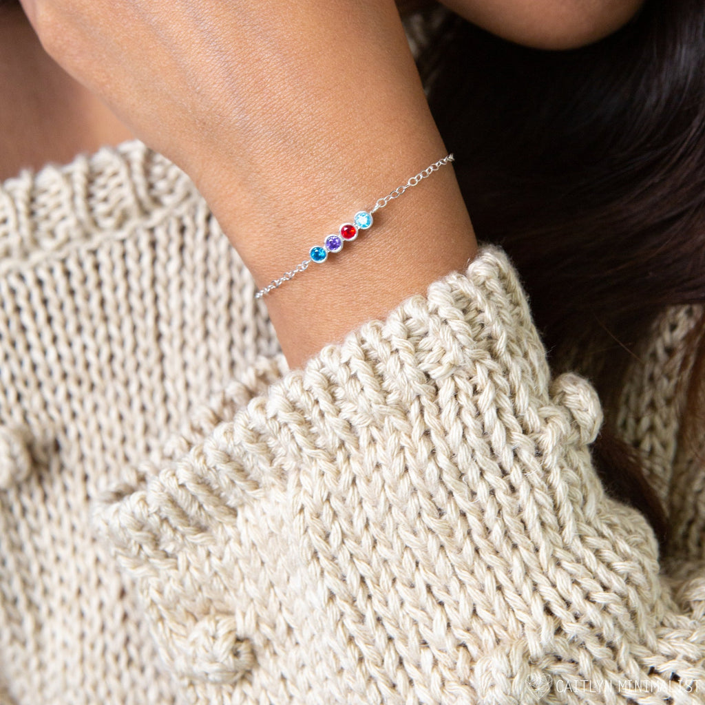 A close-up of a woman's wrist wearing the Multiple Birthstone Bracelet, a delicate sterling silver piece featuring four colorful personalized birthstones.