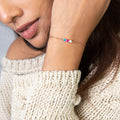 A woman wears a beige knit sweater and a Multiple Birthstone Bracelet, featuring three colorful personalized birthstones.