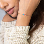 A woman wears a beige knit sweater and a Multiple Birthstone Bracelet, featuring three colorful personalized birthstones.
