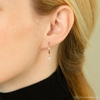 Close-up of a woman's ear wearing Birthstone Huggies, featuring a delicate gold hoop with a dangling round diamond—perfect for those who love personalized earrings.
