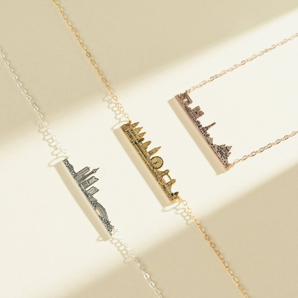 Three City Skyline Necklaces in silver, gold, and rose gold rest on a neutral background—an elegant accessory and thoughtful personalized gift.
