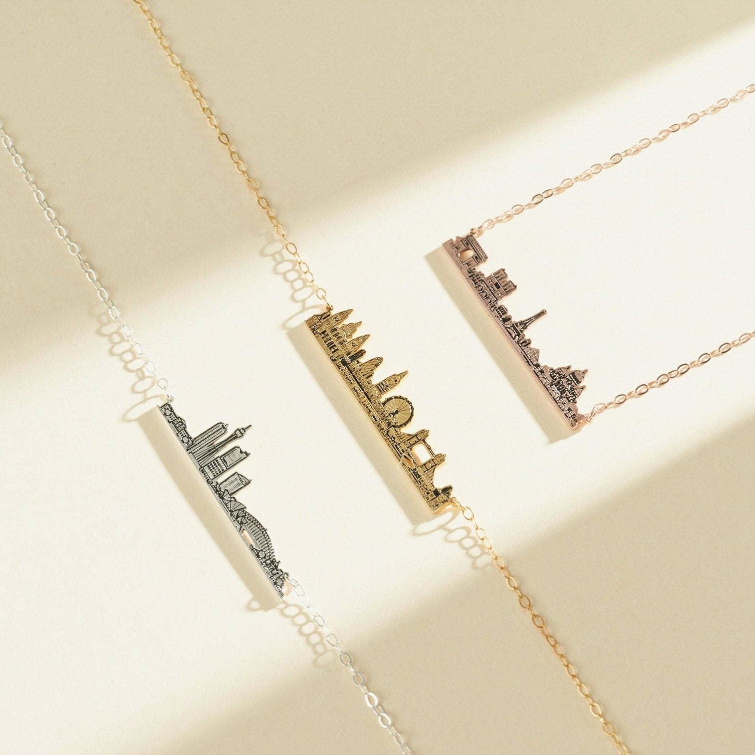 Three City Skyline Necklaces in silver, gold, and rose gold rest on a neutral background—an elegant accessory and thoughtful personalized gift.