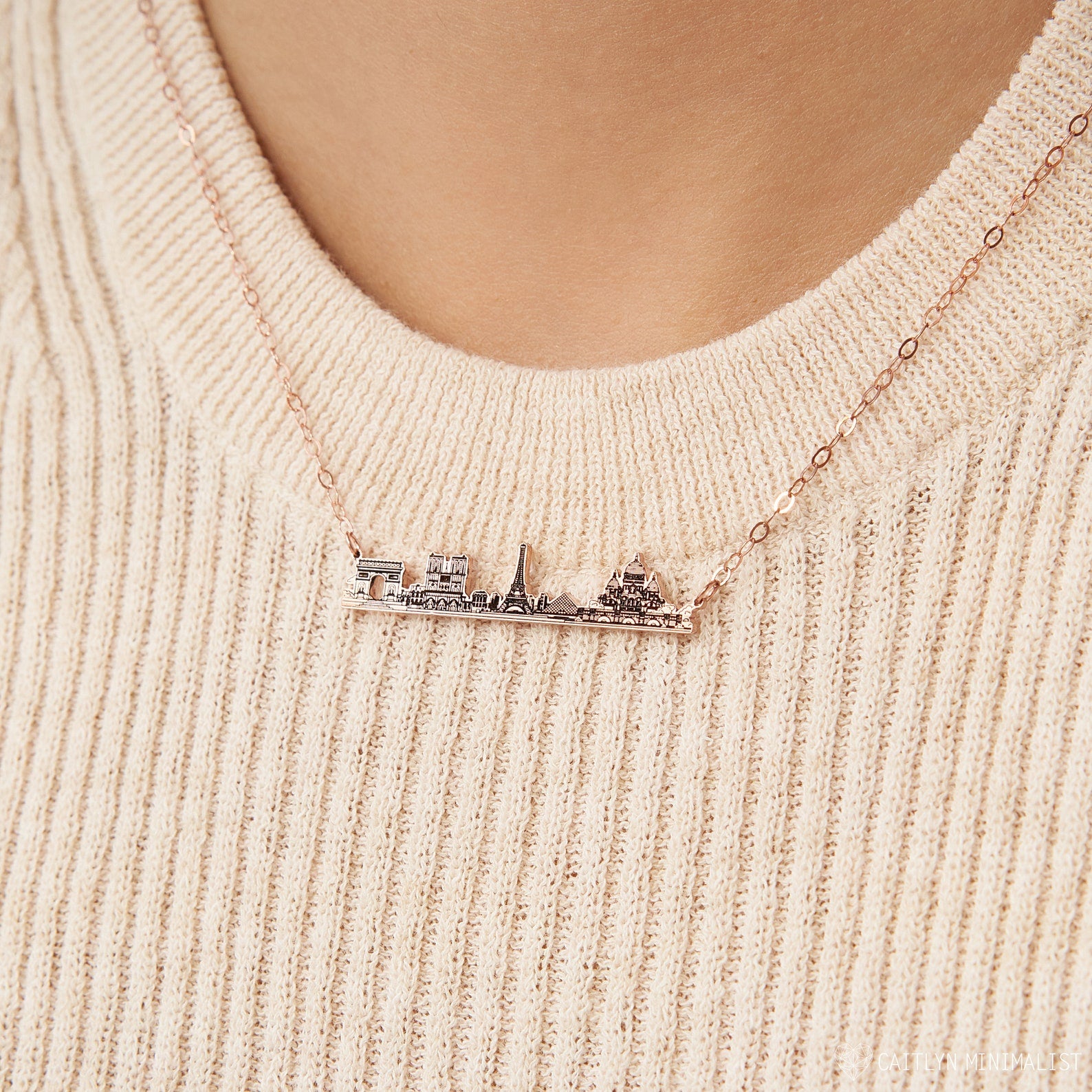 A person wearing a cozy cream knit sweater and the City Skyline Necklace, creating a stylish, personalized gift idea.