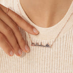 A hand adjusts the City Skyline Necklace, featuring a cityscape pendant, worn over a cream ribbed sweater—an ideal personalized gift.