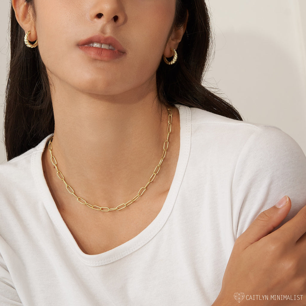 Woman wearing a white shirt, gold hoop earrings, and a boho-chic layered look featuring the Paperclip Toggle Necklace in Rose Gold, set against a neutral background.