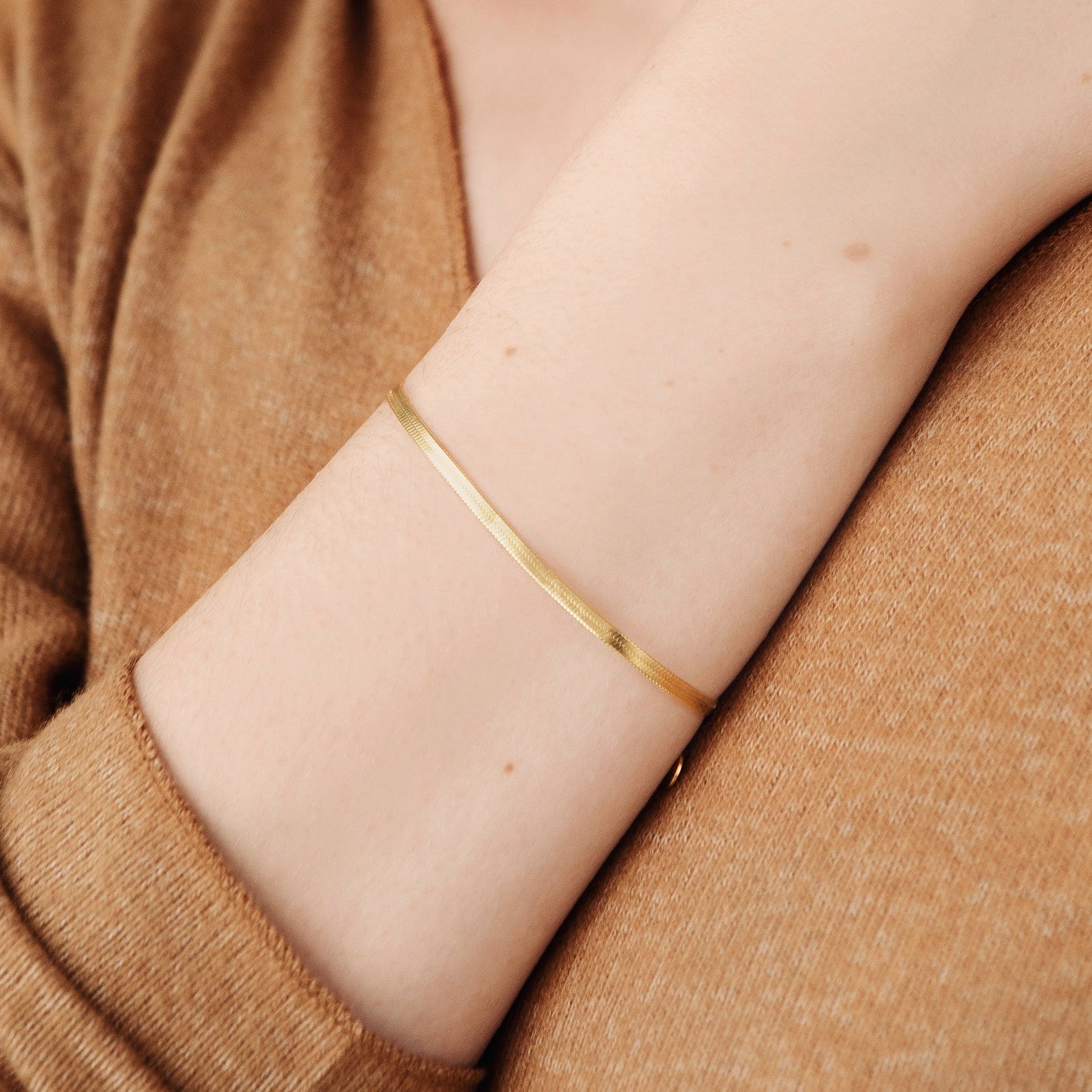 The Herringbone Bracelet elegantly drapes on the wrist, styled with a light brown long-sleeve top for a modern look.