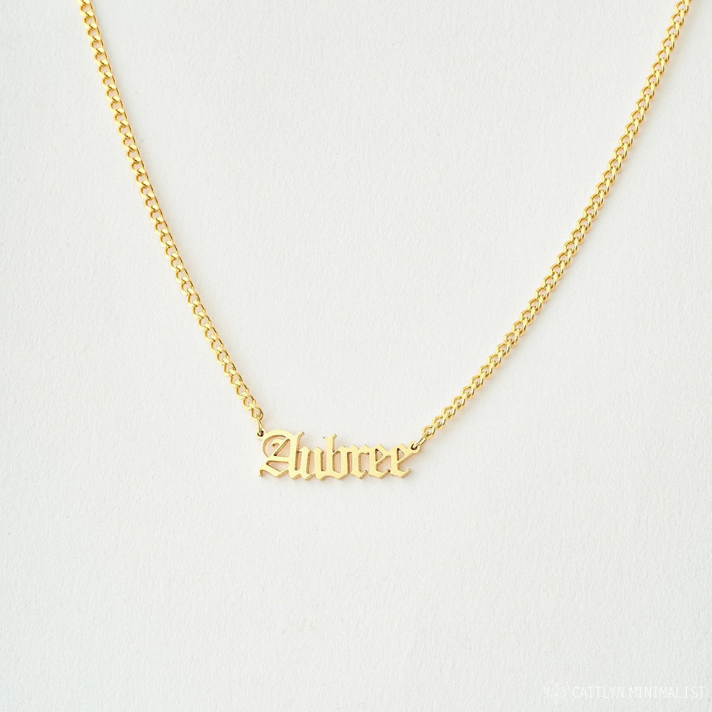 Old English Name Necklace in Curb Chain features the name Aubree in a stylish old English font on a white background, with a personalized charm and elegant curb chain for added style.