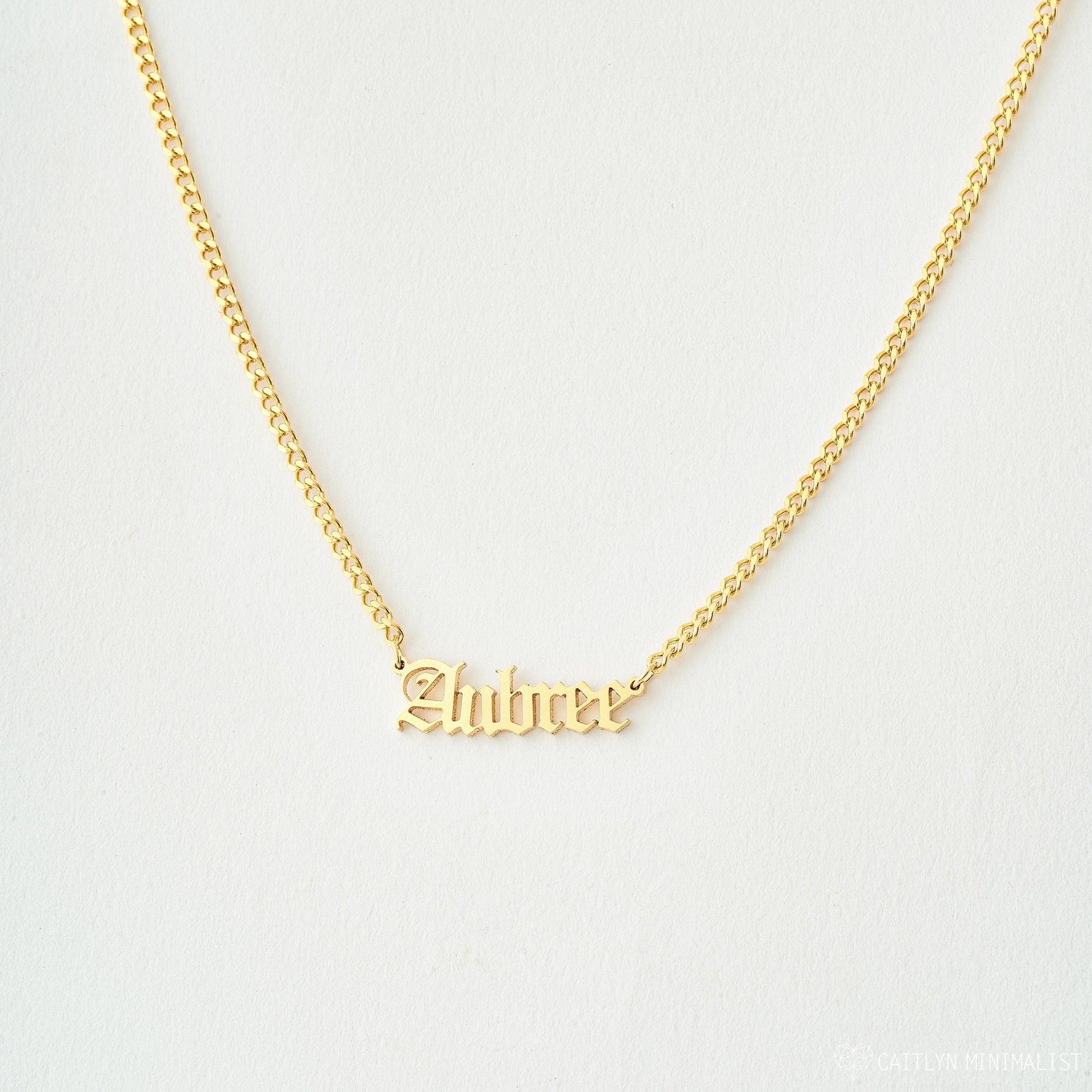 Old English Name Necklace in Curb Chain features the name Aubree in a stylish old English font on a white background, with a personalized charm and elegant curb chain for added style.