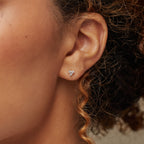 Close-up of a woman's ear wearing Mini Lily Studs—delicate diamond earrings featuring three stones, ideal for everyday wear or pairing with cartilage piercings.