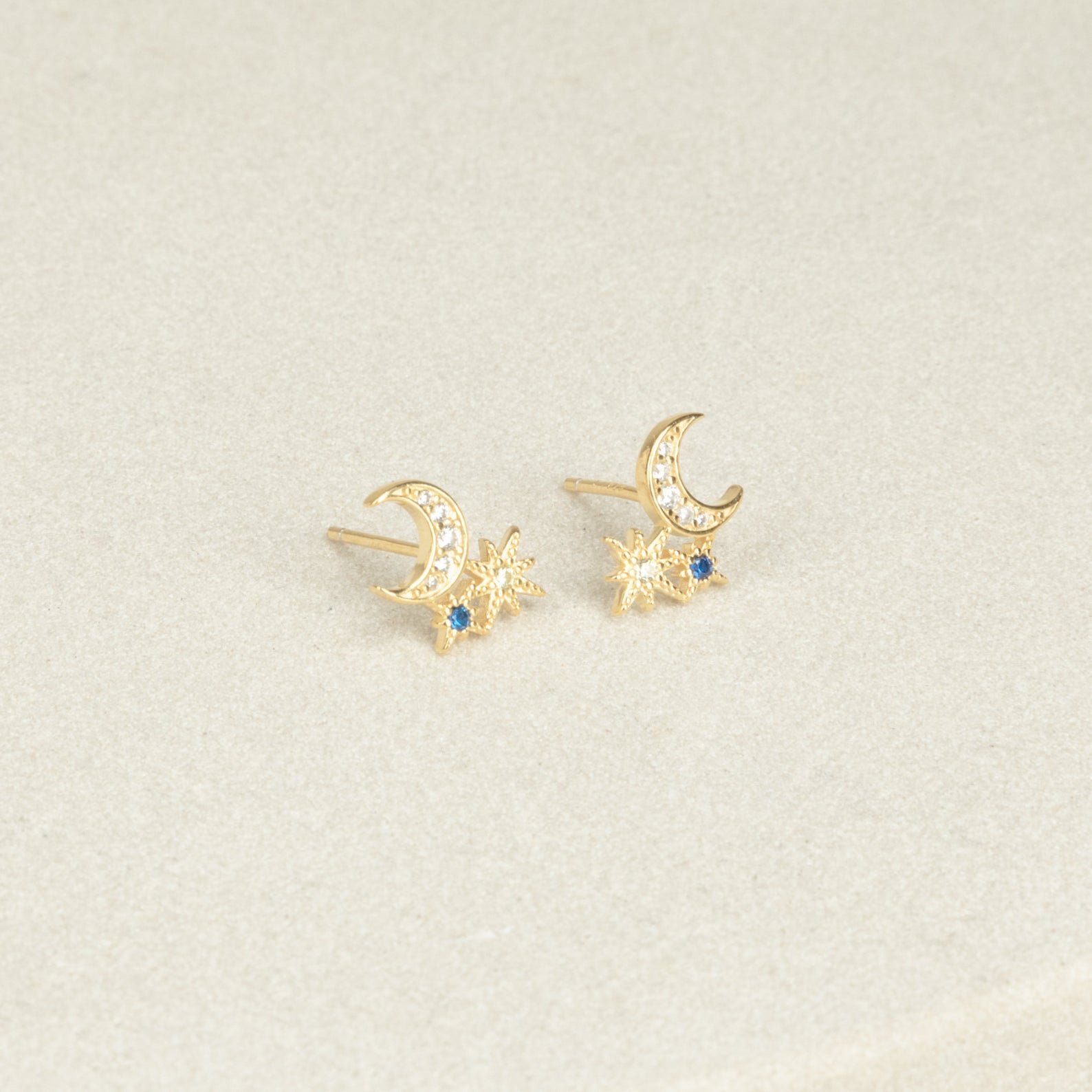 The Aeon Studs feature gold constellations with crescent moons, star shapes, and sapphire accents that bring celestial charm to any neutral backdrop.