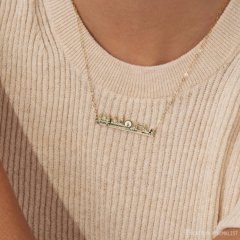 The City Skyline Necklace features an urban skyline pendant, styled over a beige ribbed top—a unique cityscape necklace and thoughtful personalized gift.