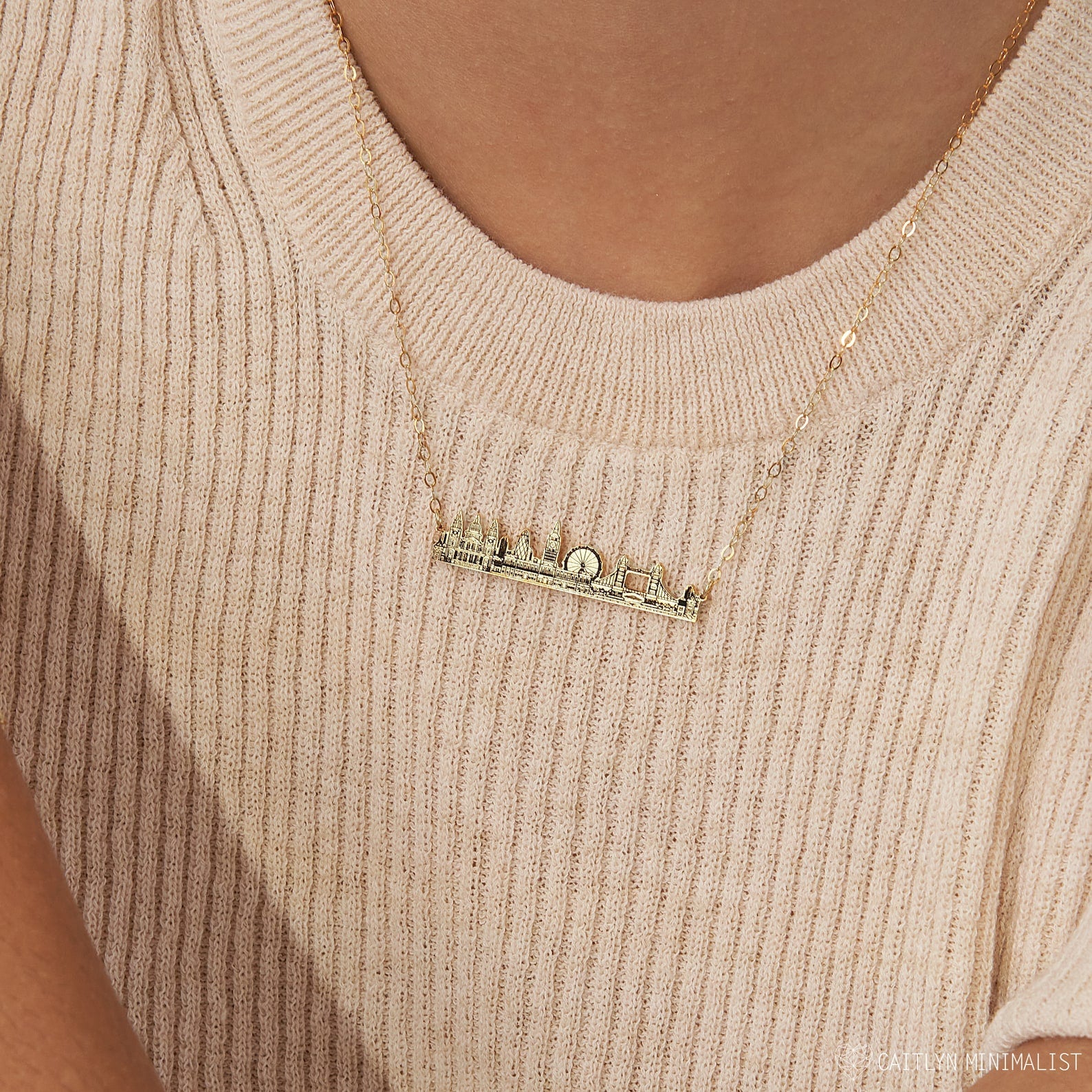 The City Skyline Necklace features an urban skyline pendant, styled over a beige ribbed top—a unique cityscape necklace and thoughtful personalized gift.