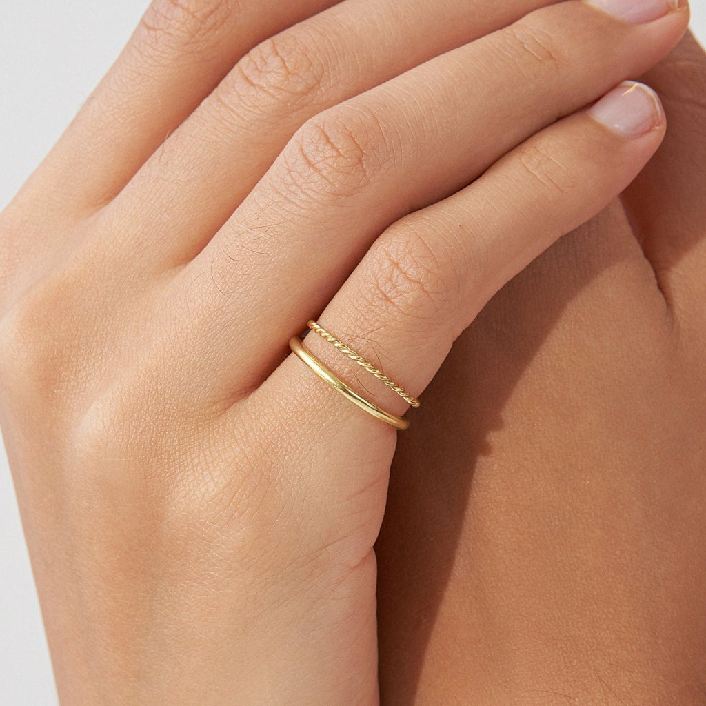 A hand wearing two thin gold bands—one plain, one with a delicate chain design—showcases the Minimalist Stacking Ring Set, perfect for everyday elegance.