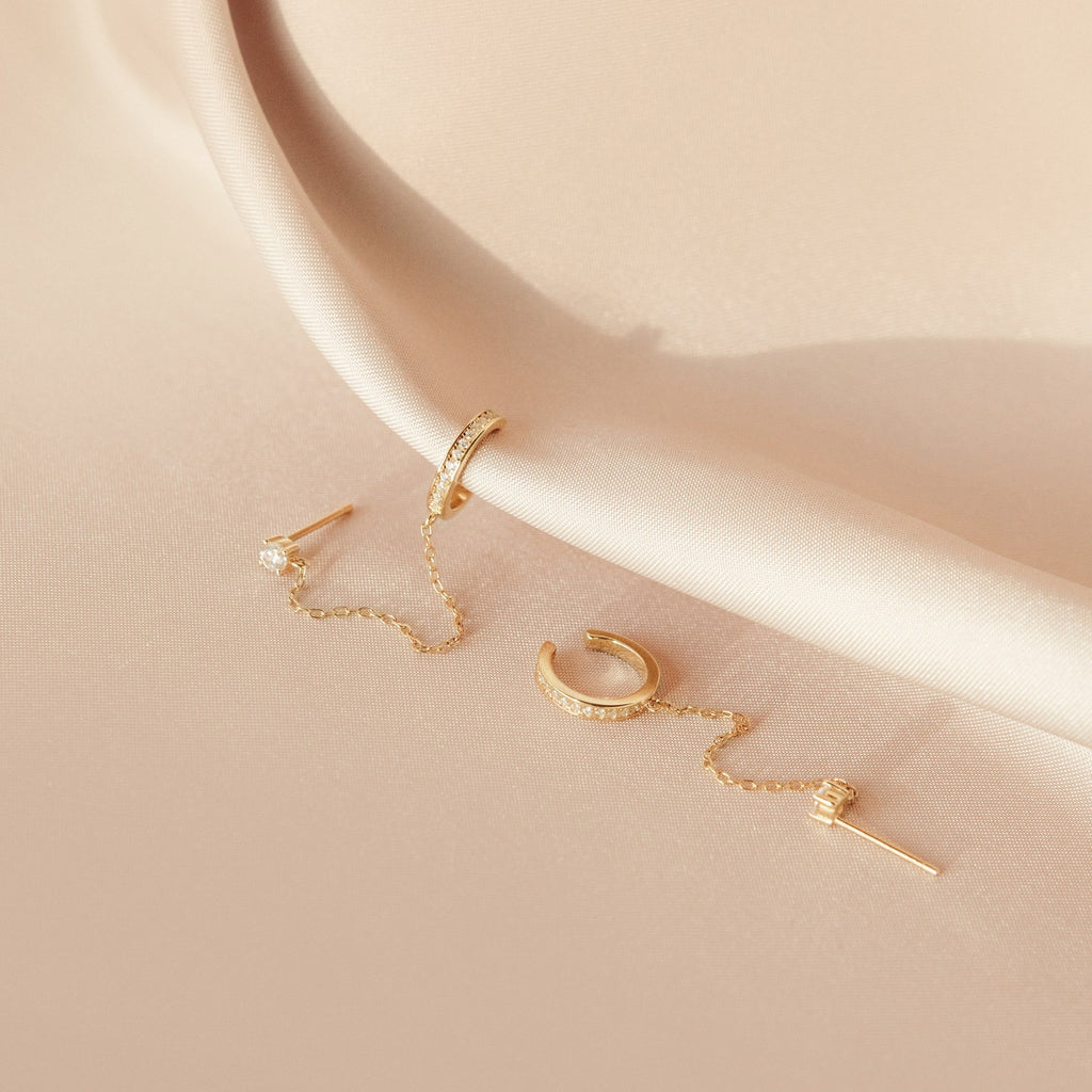 Pave Chain Ear Cuffs elegantly displayed on pale, silky fabric feature a delicate chain for a refined look.