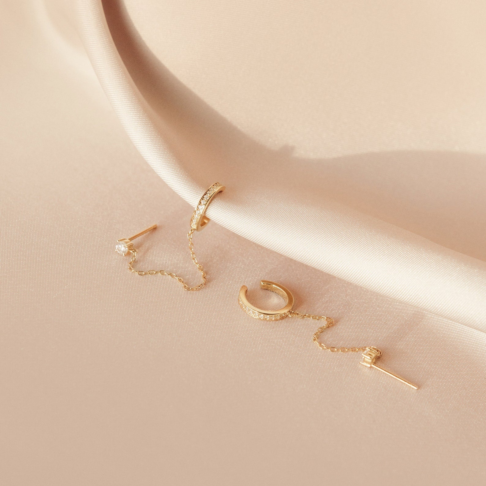 Pave Chain Ear Cuffs elegantly displayed on pale, silky fabric feature a delicate chain for a refined look.