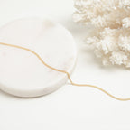 A gold curb chain necklace styled on a white marble round tray next to white coral, arranged in a flowing curve.