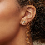 Close-up of a woman's ear adorned with Aeon Studs, gold stars shining beside crescent moon earrings, her curly hair softly framing the constellation-inspired look.
