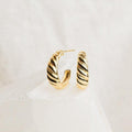 Croissant Hoops—gold twisted earrings with elegant detailing—displayed on a white textured surface.