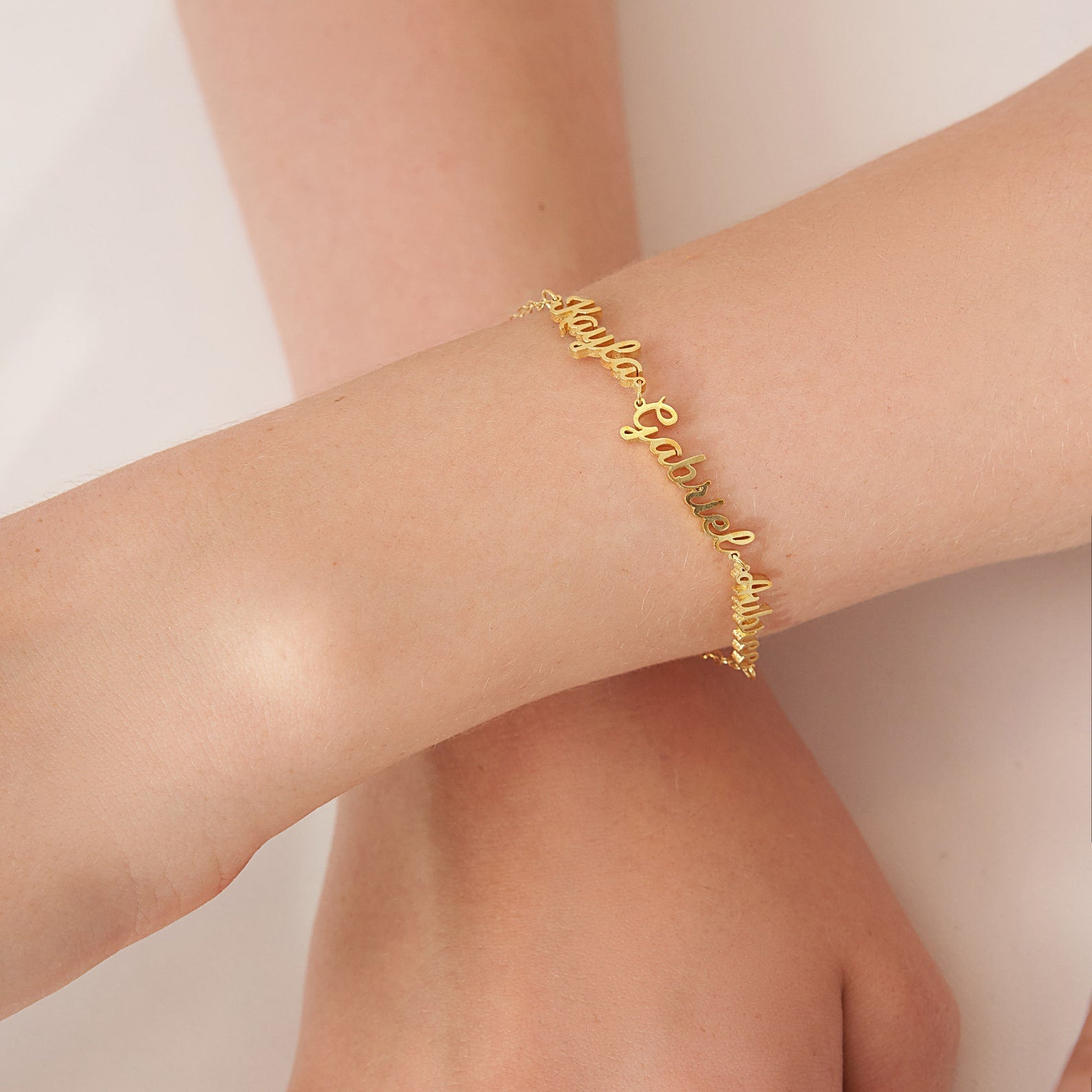The Classic Multiple Name Bracelet features a dainty chain with names in elegant script, shown on a wrist against a neutral background—a lovely piece of personalized jewelry.
