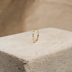 The Baguette Eternity Ring, featuring slim gold and rectangular baguette diamonds, is displayed on a textured concrete block with a beige backdrop, reflecting modern luxury.