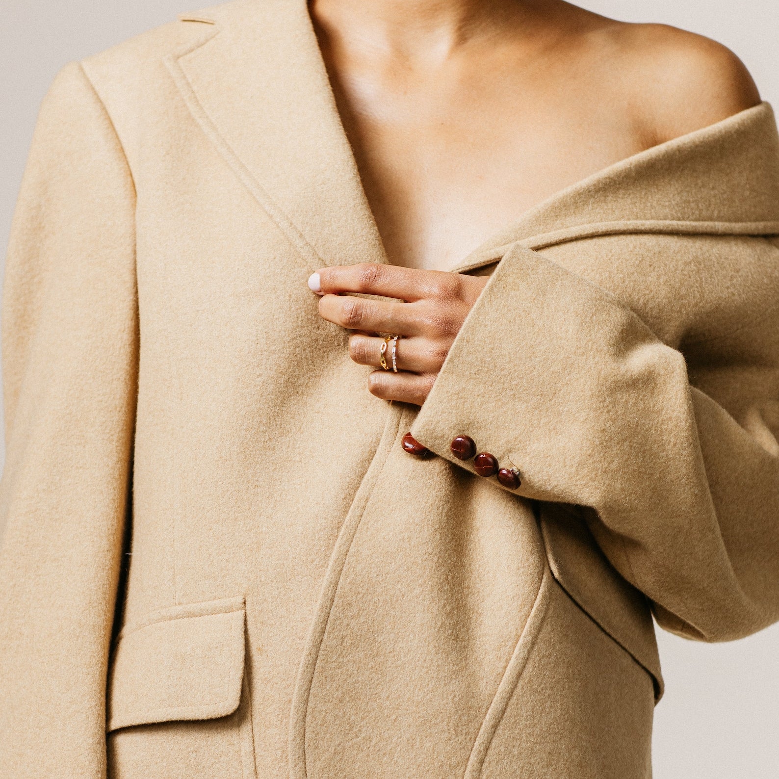 A person wears an oversized beige blazer off one shoulder, showcasing bare skin and rings—spotlighting modern luxe style with the Baguette Eternity Ring.