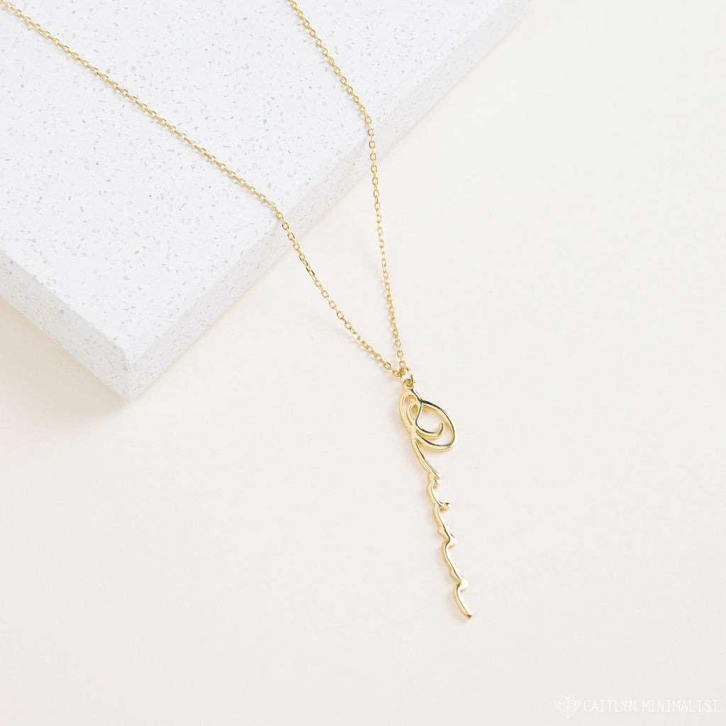 Vertical Minimal Name Necklace featuring a delicate chain and an abstract, wavy amulet pendant, displayed on a white textured surface.