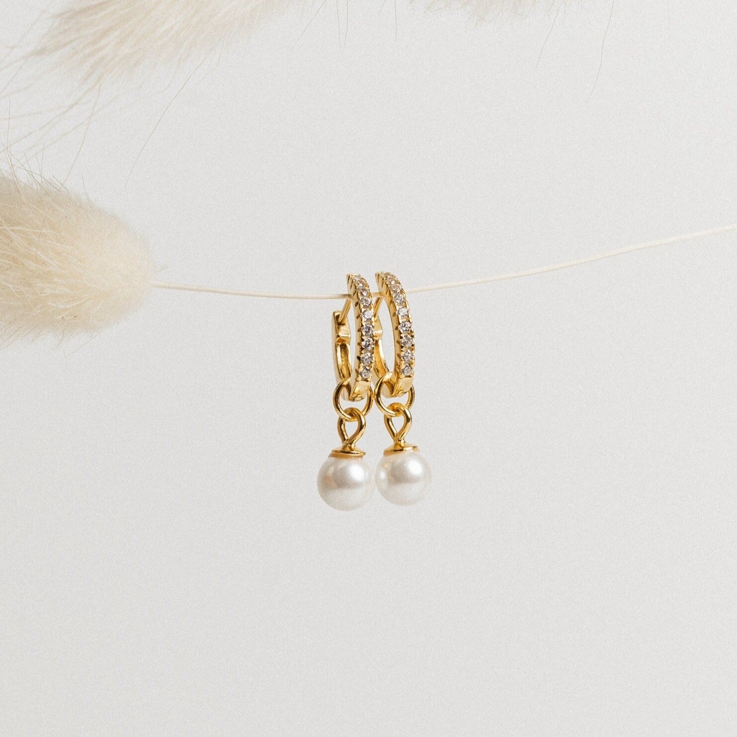 Mae Huggies: Elegant gold pearl earrings with sparkling crystals, delicately hanging on a string against a light background.