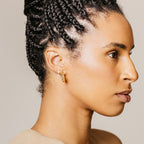 A woman with braided hair wears the Lexi Flower Studs—delicate gold and diamond earrings—while looking to the right against a neutral background.