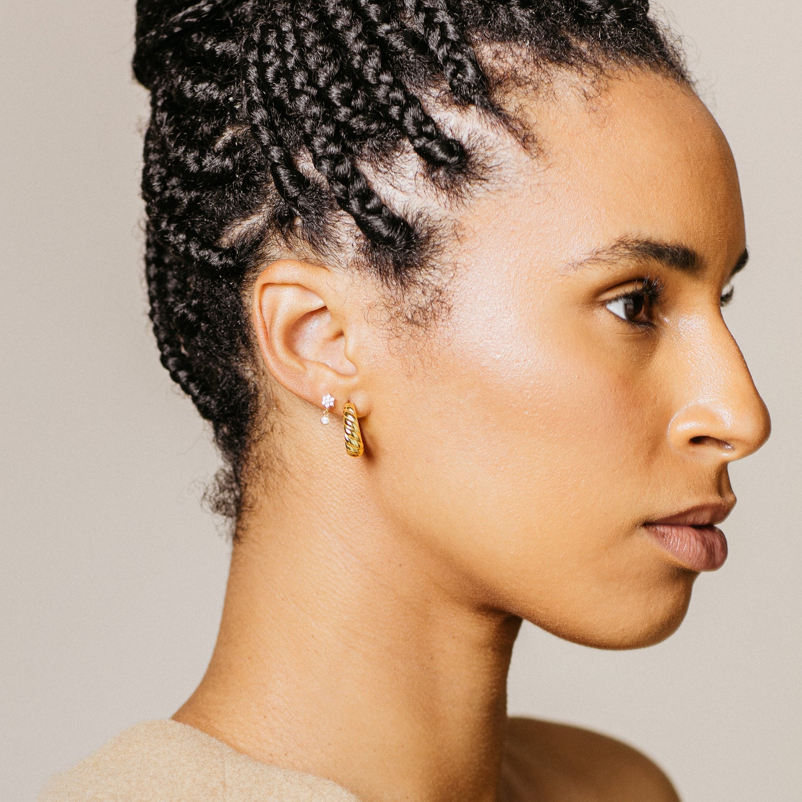 A woman with braided hair wears the Lexi Flower Studs—delicate gold and diamond earrings—while looking to the right against a neutral background.