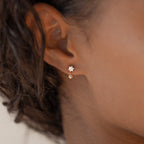 Close-up of an ear adorned with Lexi Flower Studs, featuring dainty floral design and a small dangling gemstone for a subtle touch of elegance.