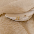 Lexi Flower Studs featuring gold floral designs with small clear stones, displayed on beige textured fabric and a shell.