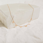 Custom Letter Necklace in Rose Gold featuring dangling charms that spell BROOKLYN, shown on a white stone block—a personalized necklace ideal for adding a unique touch.