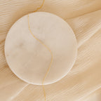 A Satellite Necklace laid across a round marble slab on a beige, crinkled fabric background.