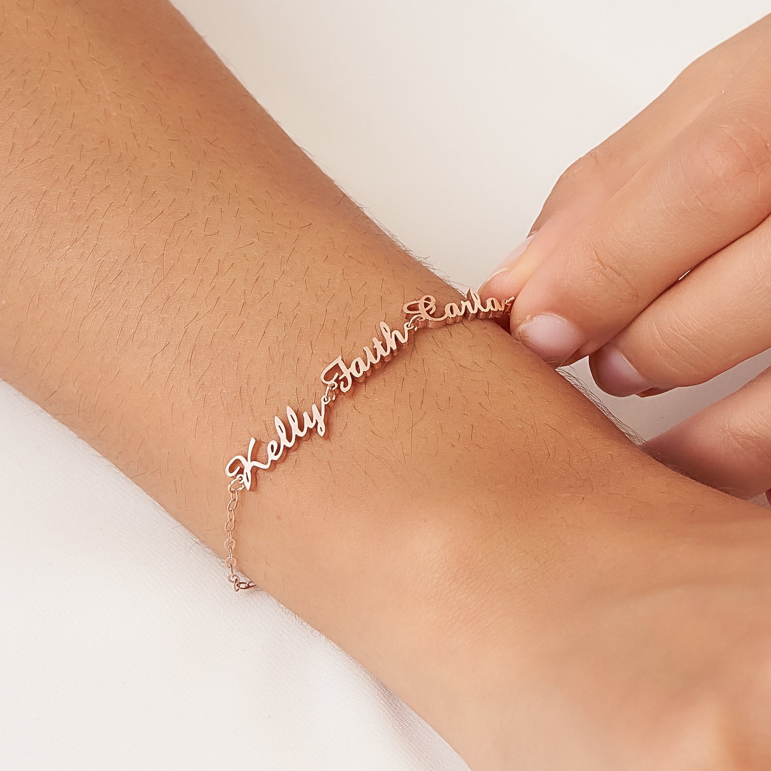 A hand fastens a Classic Multiple Name Bracelet, personalized with the names Kelly, Faith, and Carla, onto a wrist.