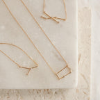 Three gold Constellation Necklaces, each inspired by the stars, are displayed on a light marble and textured stone surface.