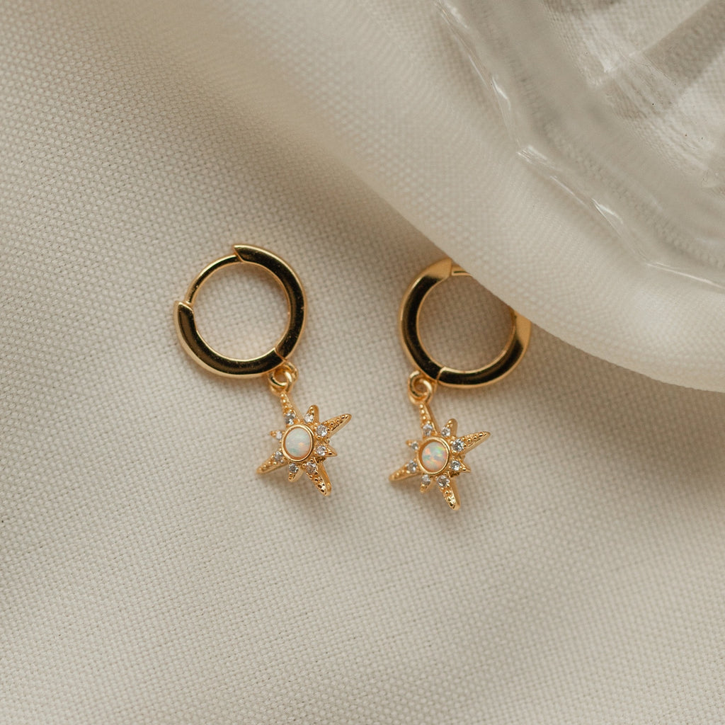 Starburst Huggies: gold hoop earrings with star-shaped, pearl center charms, displayed elegantly on soft cream fabric.