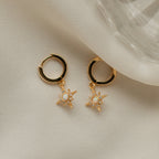 Starburst Huggies: gold hoop earrings with star-shaped, pearl center charms, displayed elegantly on soft cream fabric.