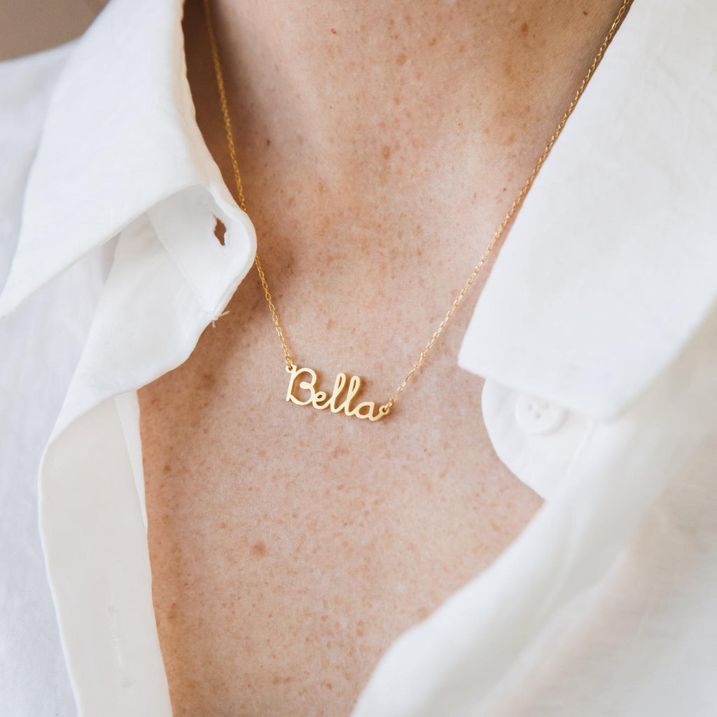 The Dainty Name Necklace gleams with a personalized touch, perfect for adding minimalist style to any outfit, like layering it over a crisp white collared shirt.