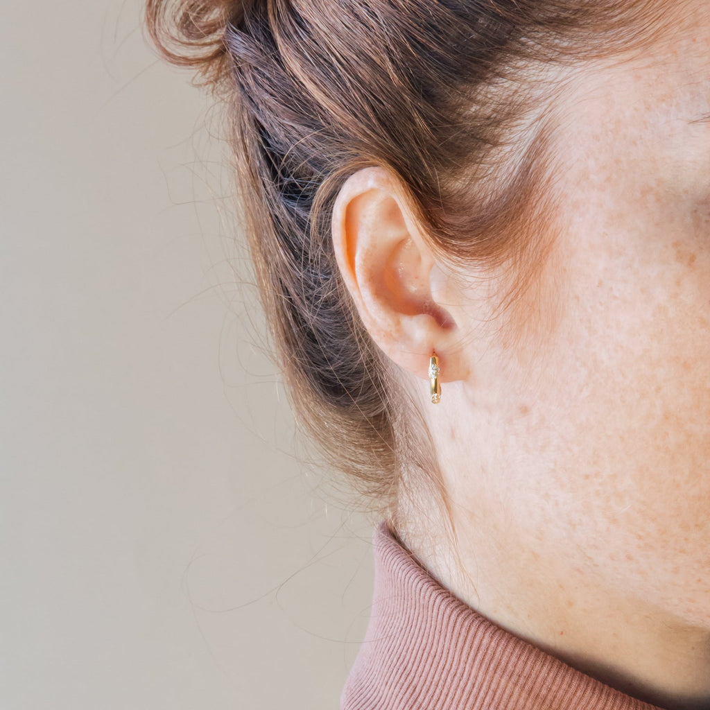 Close-up of a woman's ear wearing the Kaia Diamond Huggies, her hair tied back and dressed in a turtleneck top.