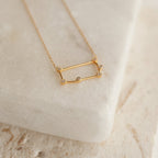 Constellation Necklace with a rectangular pendant set with small gemstones, showcased on a smooth, light-colored stone surface for a celestial look.