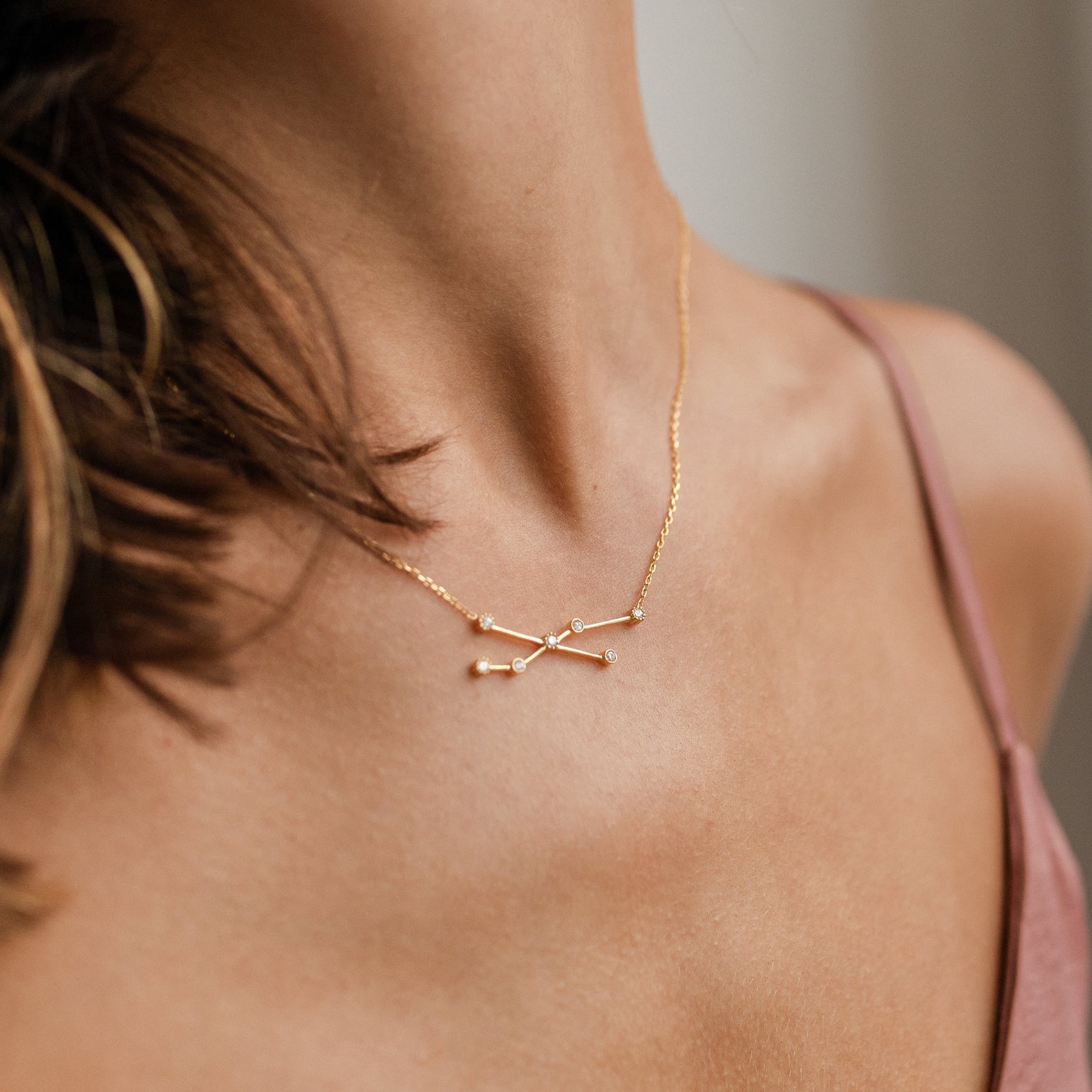 A woman wearing the Constellation Necklace, a delicate gold accessory with a minimalist design that reflects the beauty and elegance of the night sky.